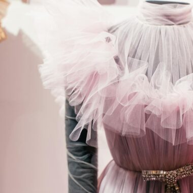 A stylish pink sheer gown with ruffled fabric showcased in a fashion studio, highlighting elegance and design.