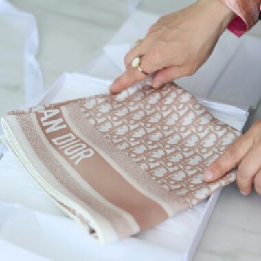 Hands gently folding a patterned luxury scarf, emphasizing delicate material and elegant design.