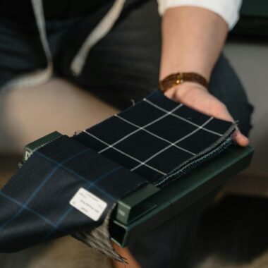 Tailor hands showcasing checkered fabric swatches for bespoke suit selection.